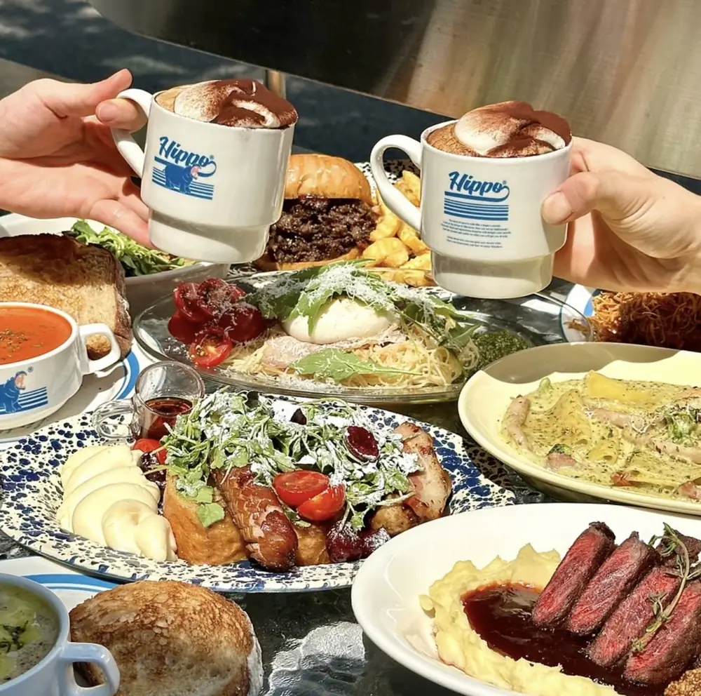 Two Hippo Vienna coffees raised over a table of brunch plates and steak at Hippo Brunchaus