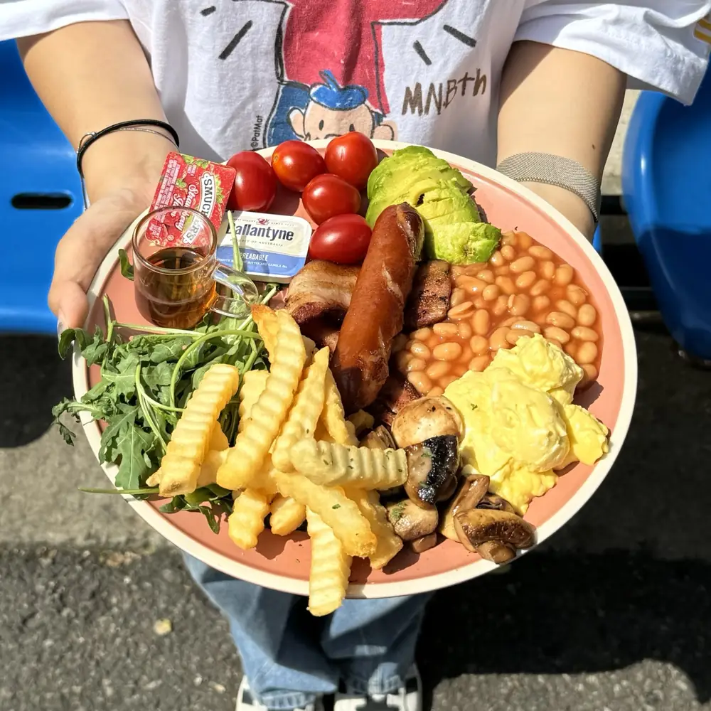 소시지·베이크드빈·스크램블에그·크링클 프라이가 담긴 브런치 플레이트를 손으로 들고 있는 모습