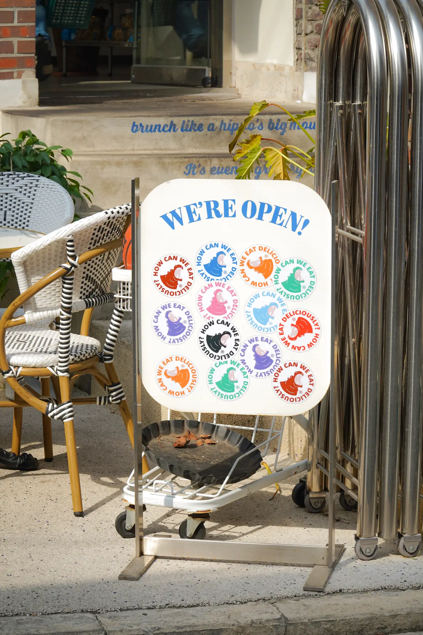 The Hippo Brunchaus terrace with rattan chairs, a 'We're open!' board and the wall line 'brunch like a hippo's big mouth'